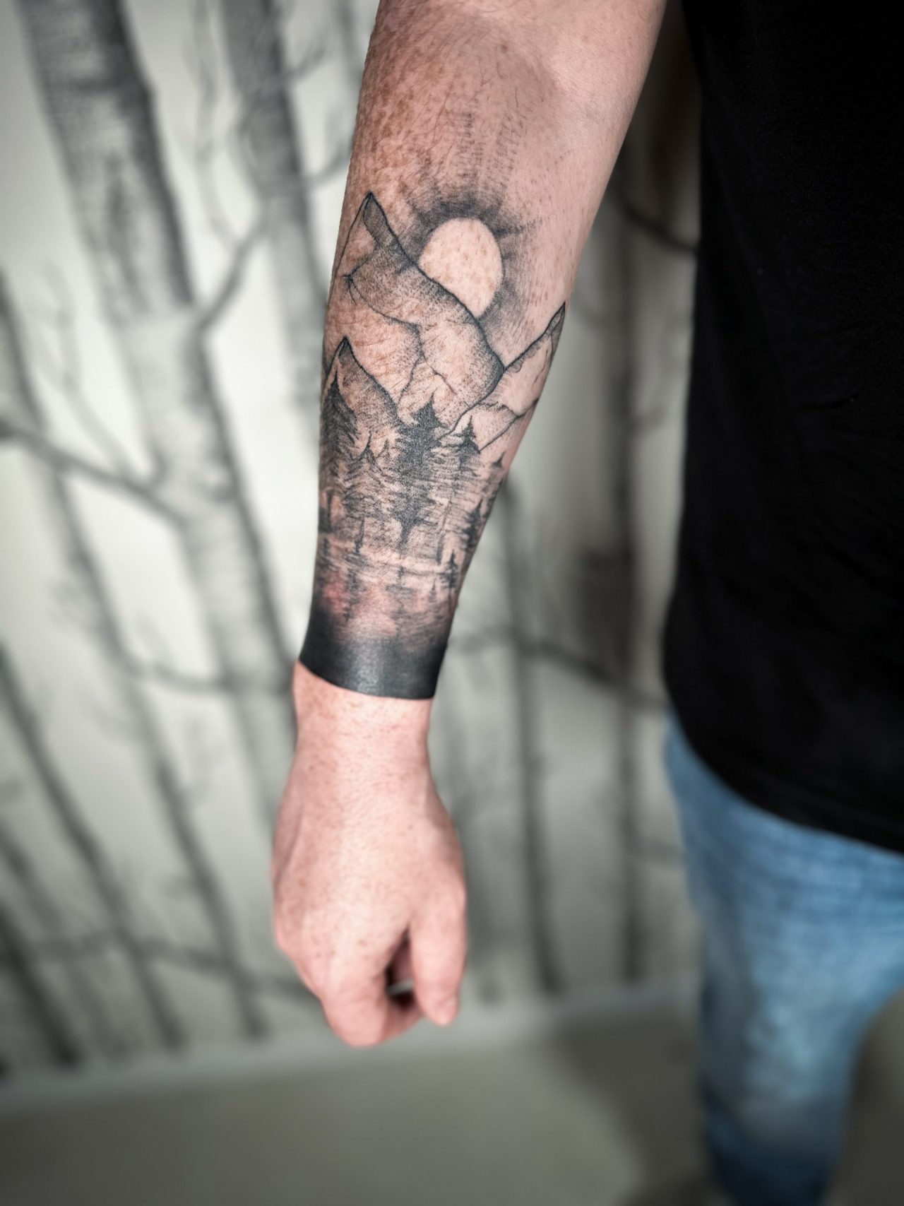Unterarmtattoo: Bergszene mit Sonne und Bäumen