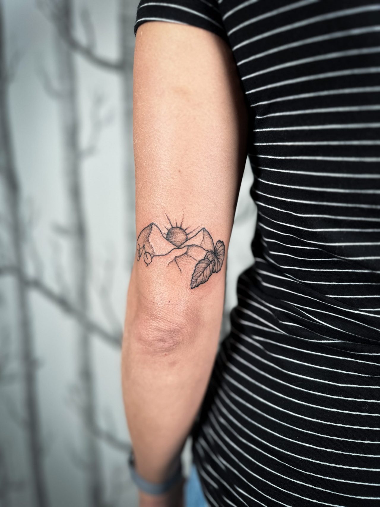 Tattoo über Ellenbogen: Berge mit Sonnenaufgang, Fahrrad und Blättern