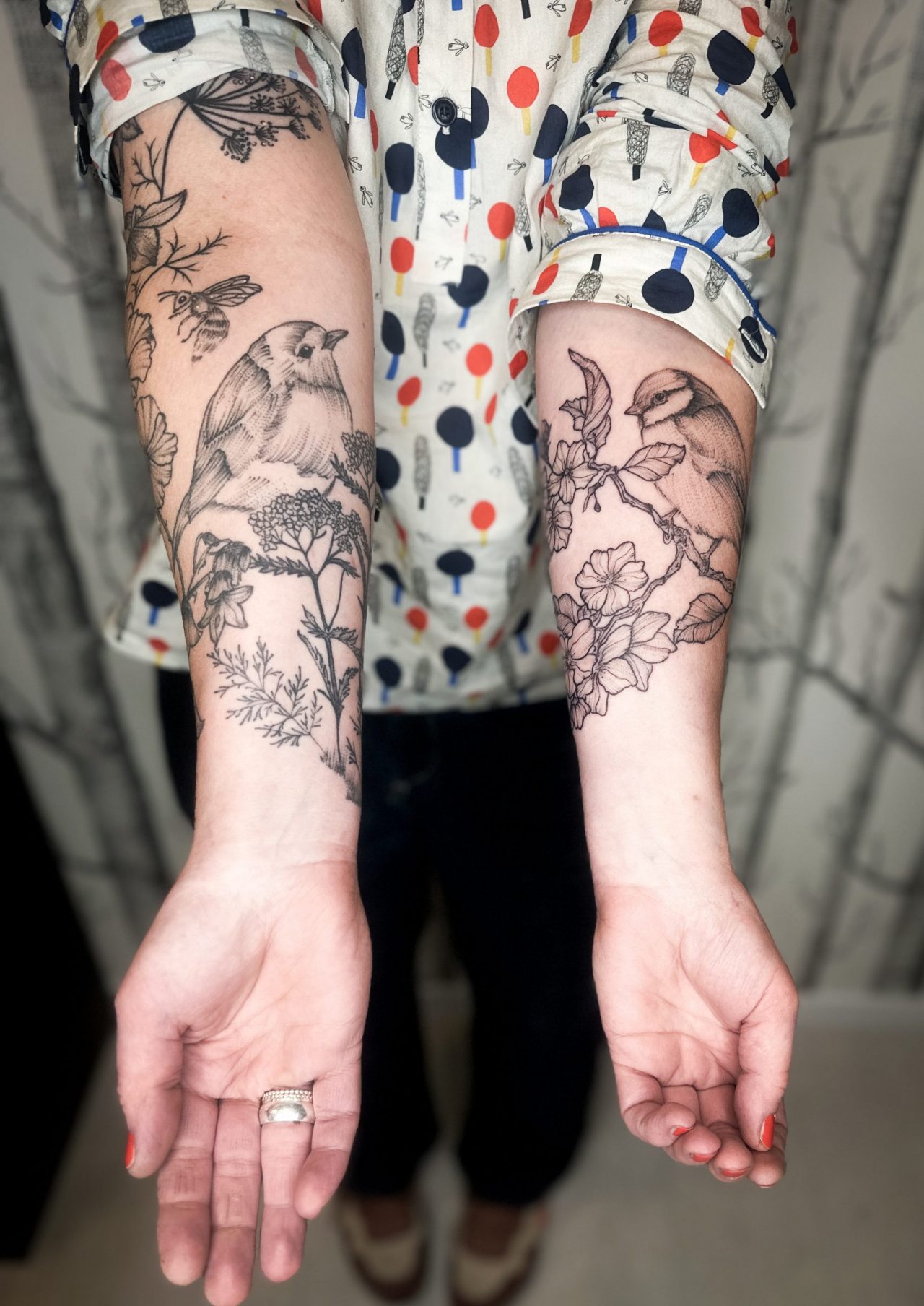 Unterarmtattoos: einmal Rotkehlchen, einmal Meise mit Blumen und Biene