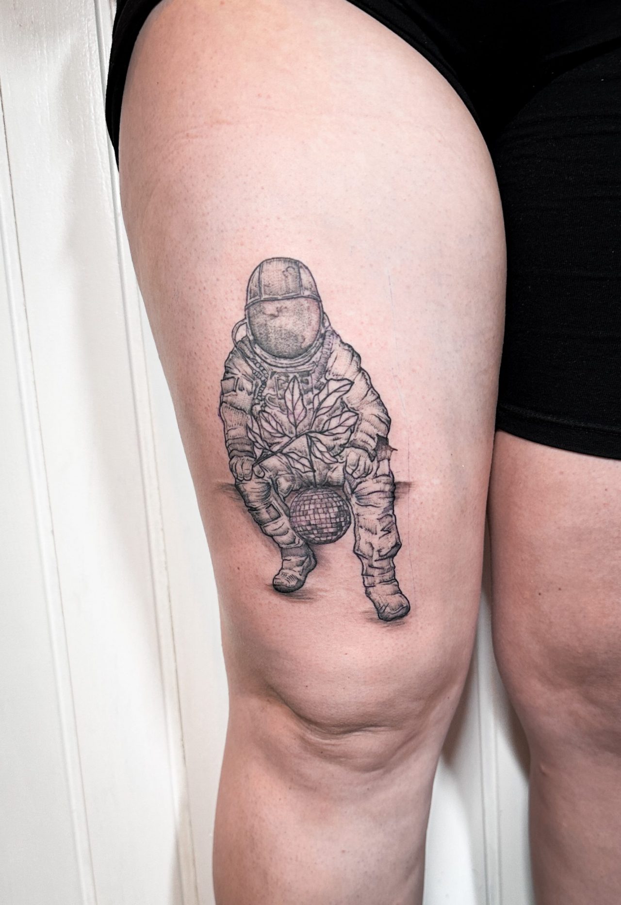 Oberschenkeltattoo: sitzender Astronaut mit Diskokugel und Vogel auf Knie