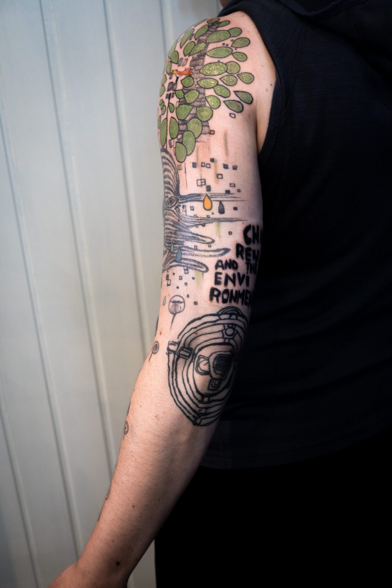 Oberarmtattoo: Hundertwasser Tattoo inspiriert von "Singender Vogel auf einem Baum in der Stadt" und "Children and the Environment"
