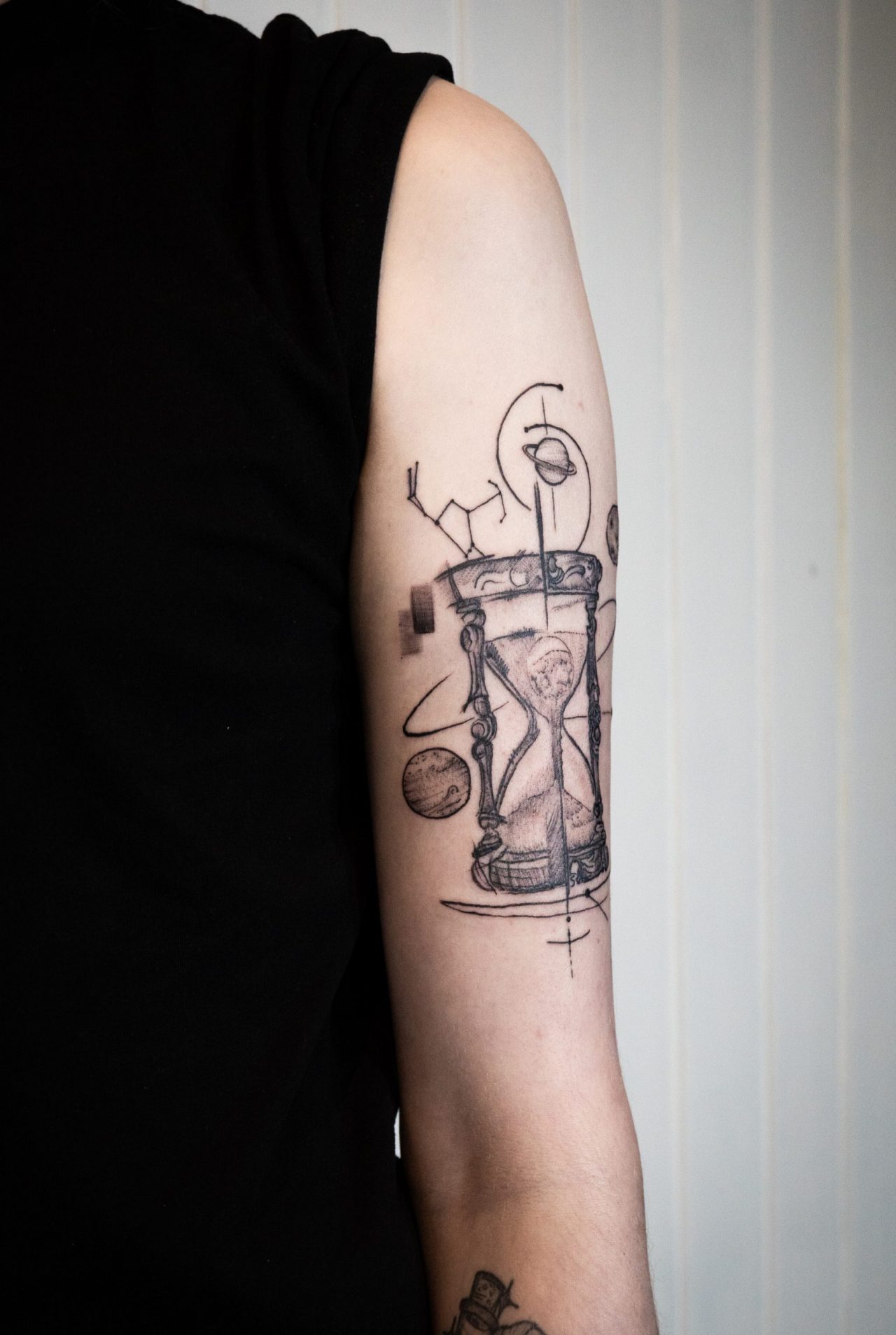 Oberarmtattoo: Sanduhr umrundet von Planeten und Sternen